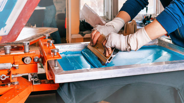 silk screen printmaking. male hands with a squeegee. serigraphy production selective focus photo. printing images on clothes by silk screen method in a design studio