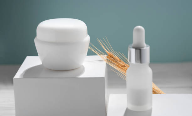 White moisturizer cream container and pipette bottle on white box with green background